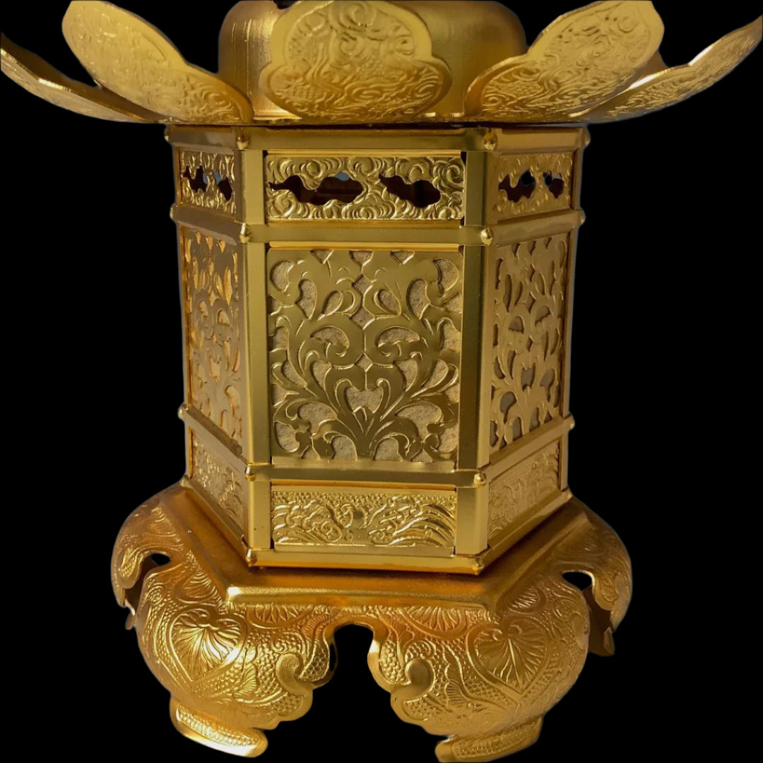Close-up of a golden Japanese lantern with elaborate floral patterns and wing-like embellishments, resting on a carved base against a dark background.