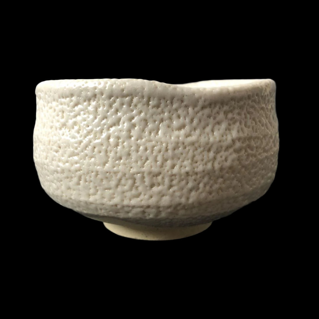 Side view of a textured white Shino ware Japanese tea bowl on a dark background.