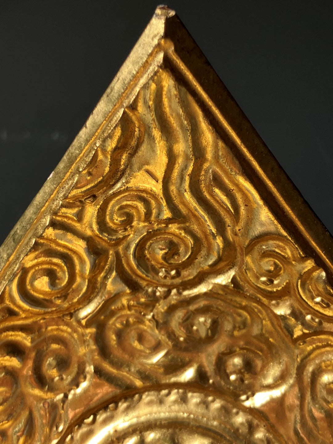 Close-up of a gold decorative object with intricate patterns on a dark background