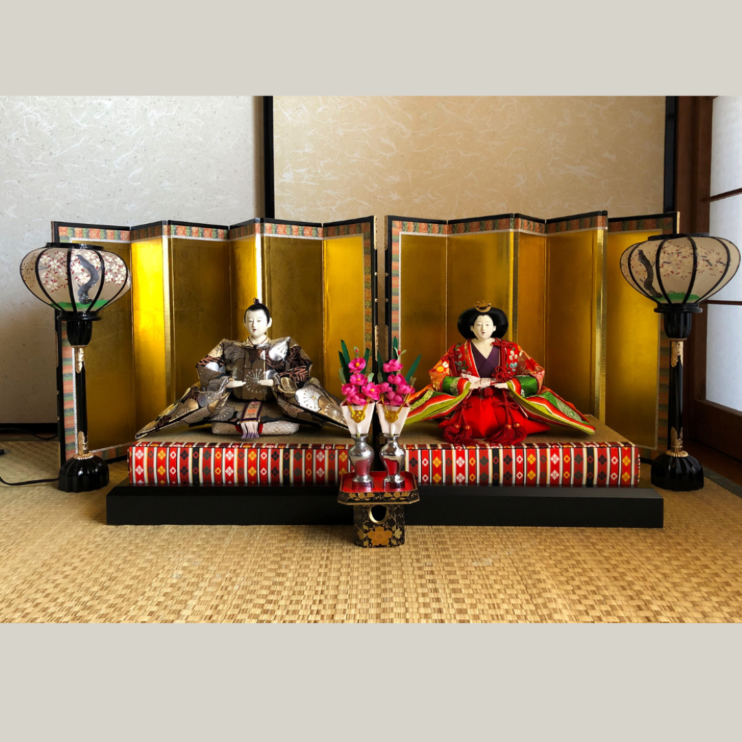 Traditional Japanese dolls in formal attire on a decorative platform with lanterns and flowers.
