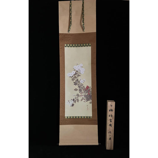 A hanging scroll with a floral painting, bordered by patterned fabric, displayed next to a wooden plank with Japanese characters, all against a black background.