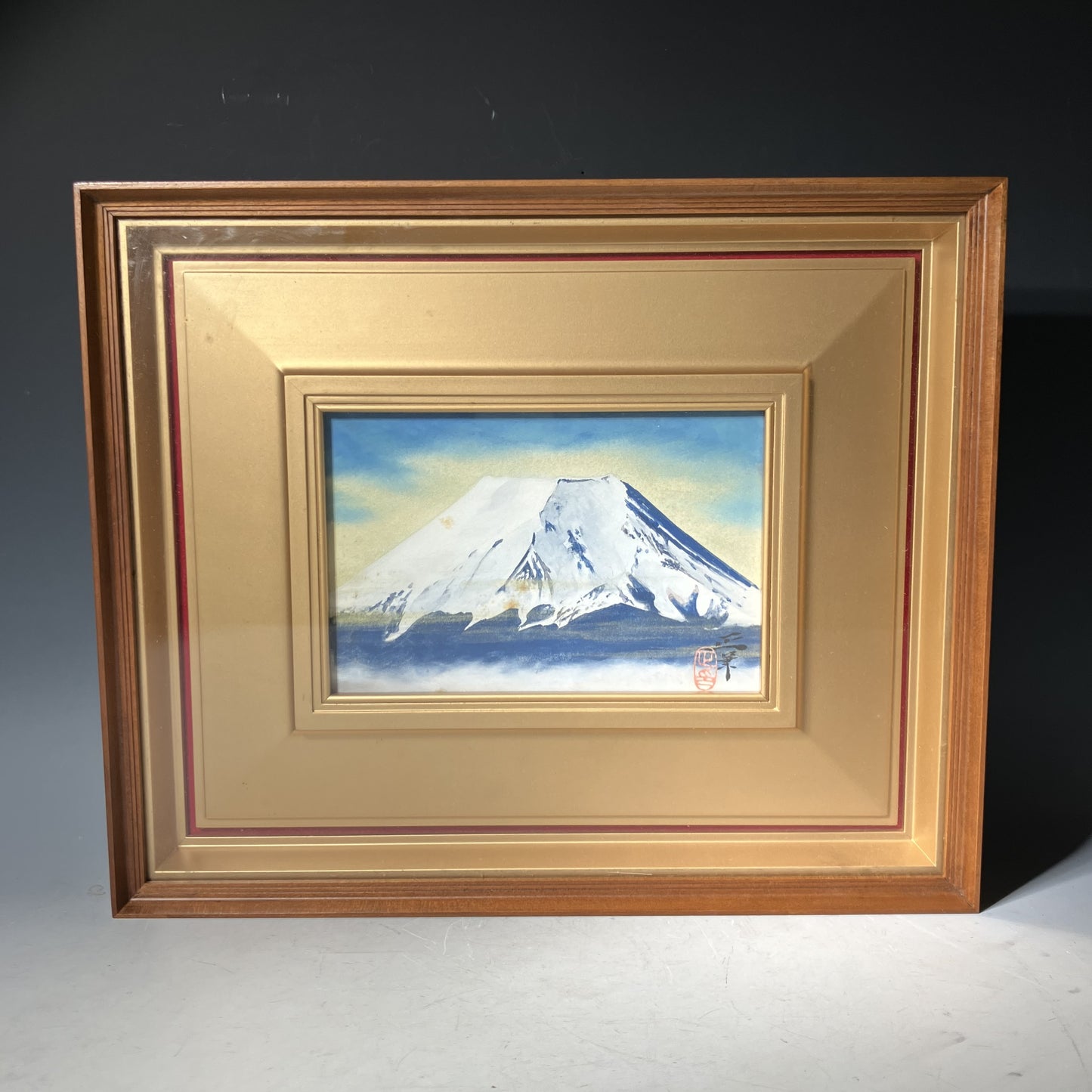 Framed painting of Mount Fuji with a gold frame on a dark background