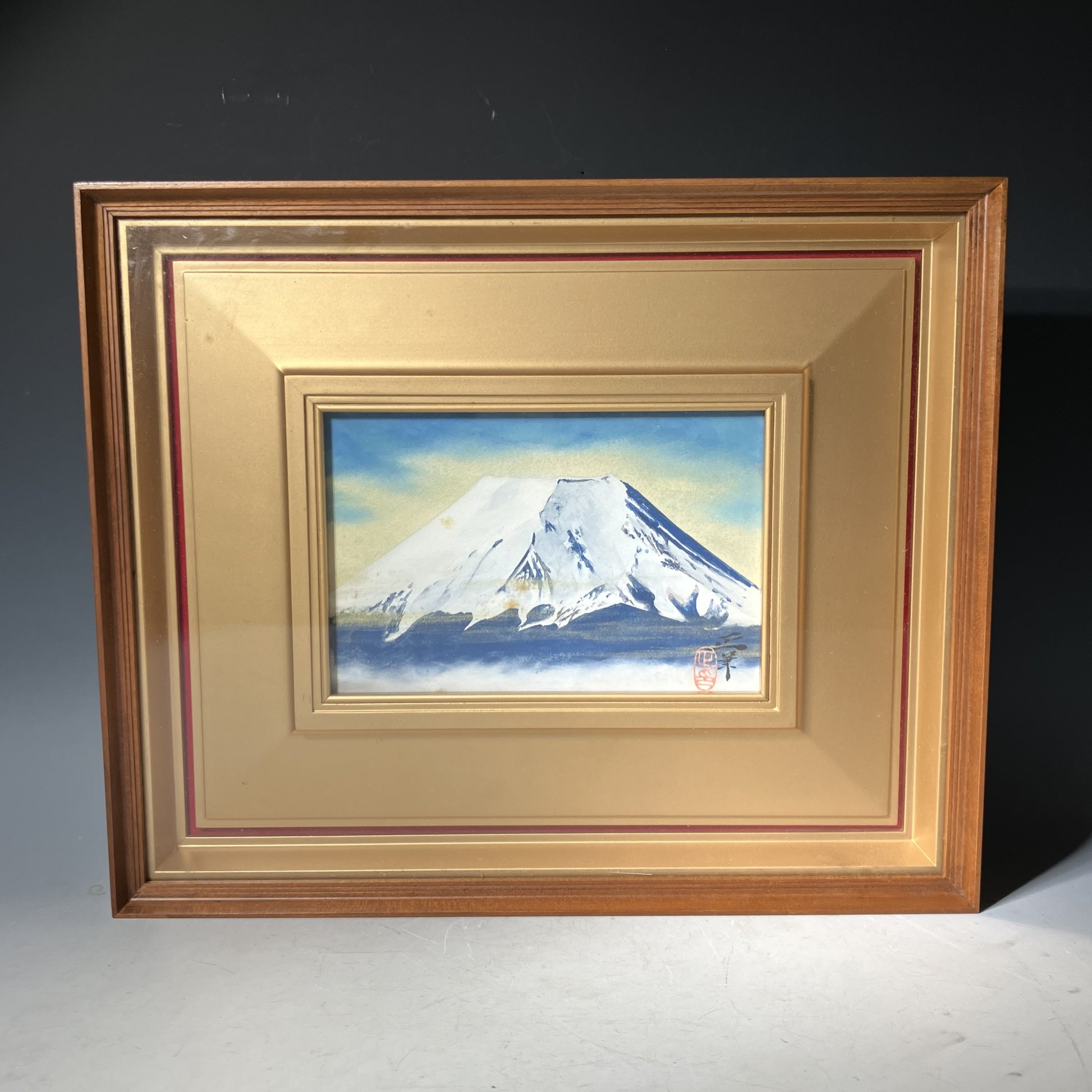 Framed painting of Mount Fuji with a gold frame on a dark background