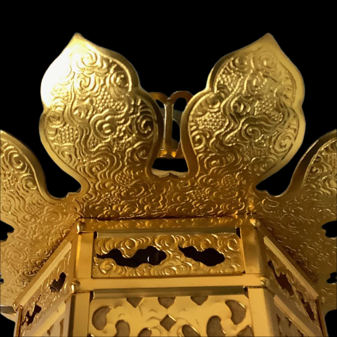 A close-up view of the top of a golden Japanese lantern, featuring ornate, embossed wing-like designs and a decorative handle.