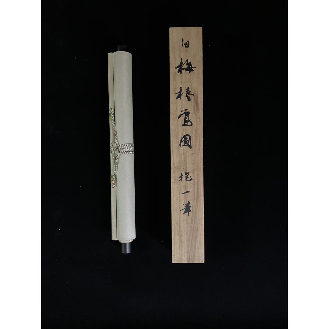A rolled-up scroll tied with a cord next to a wooden plank with Japanese calligraphy, against a black background.