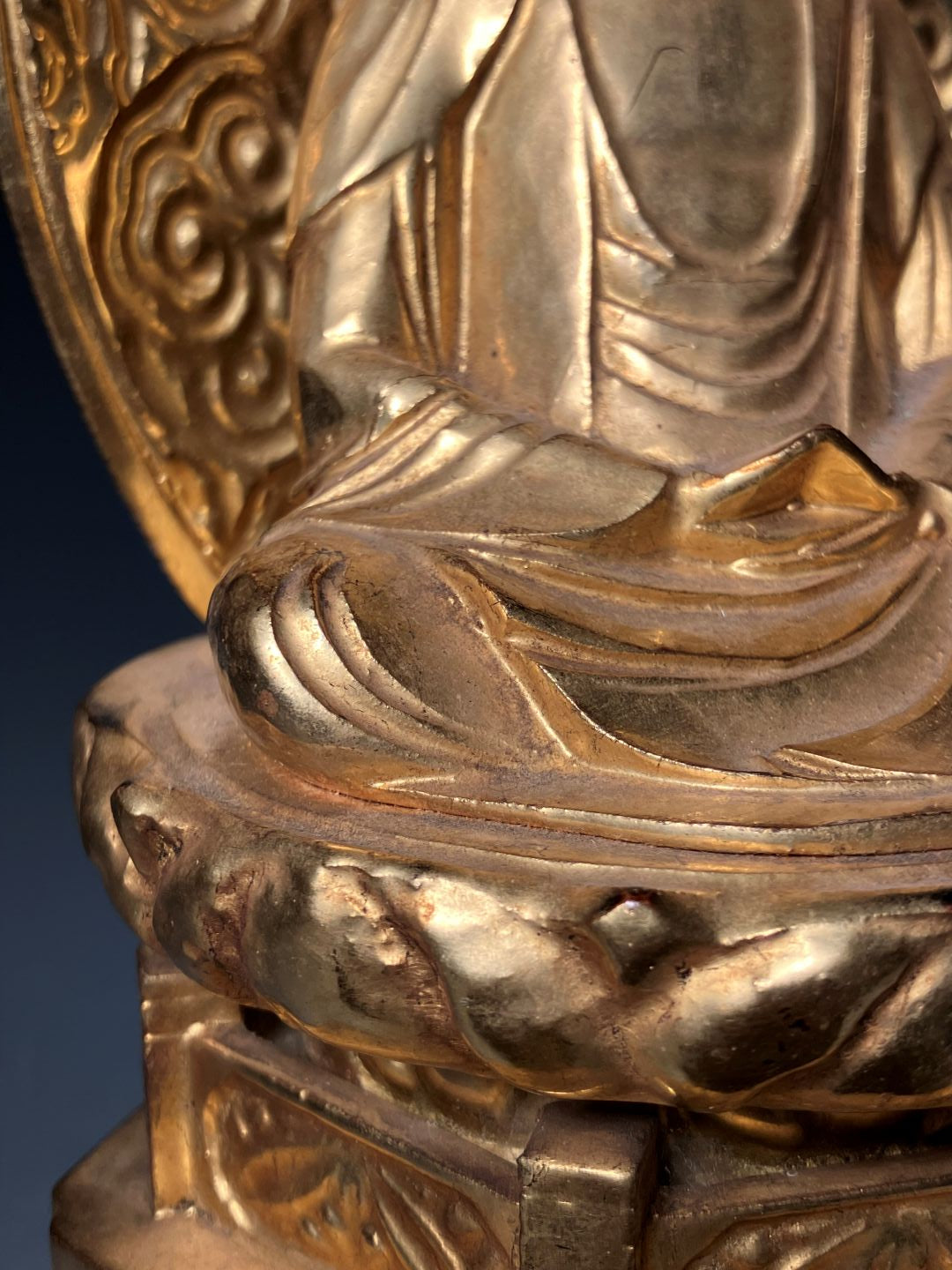 Close-up of a detailed gold figurine with intricate designs on a blue background