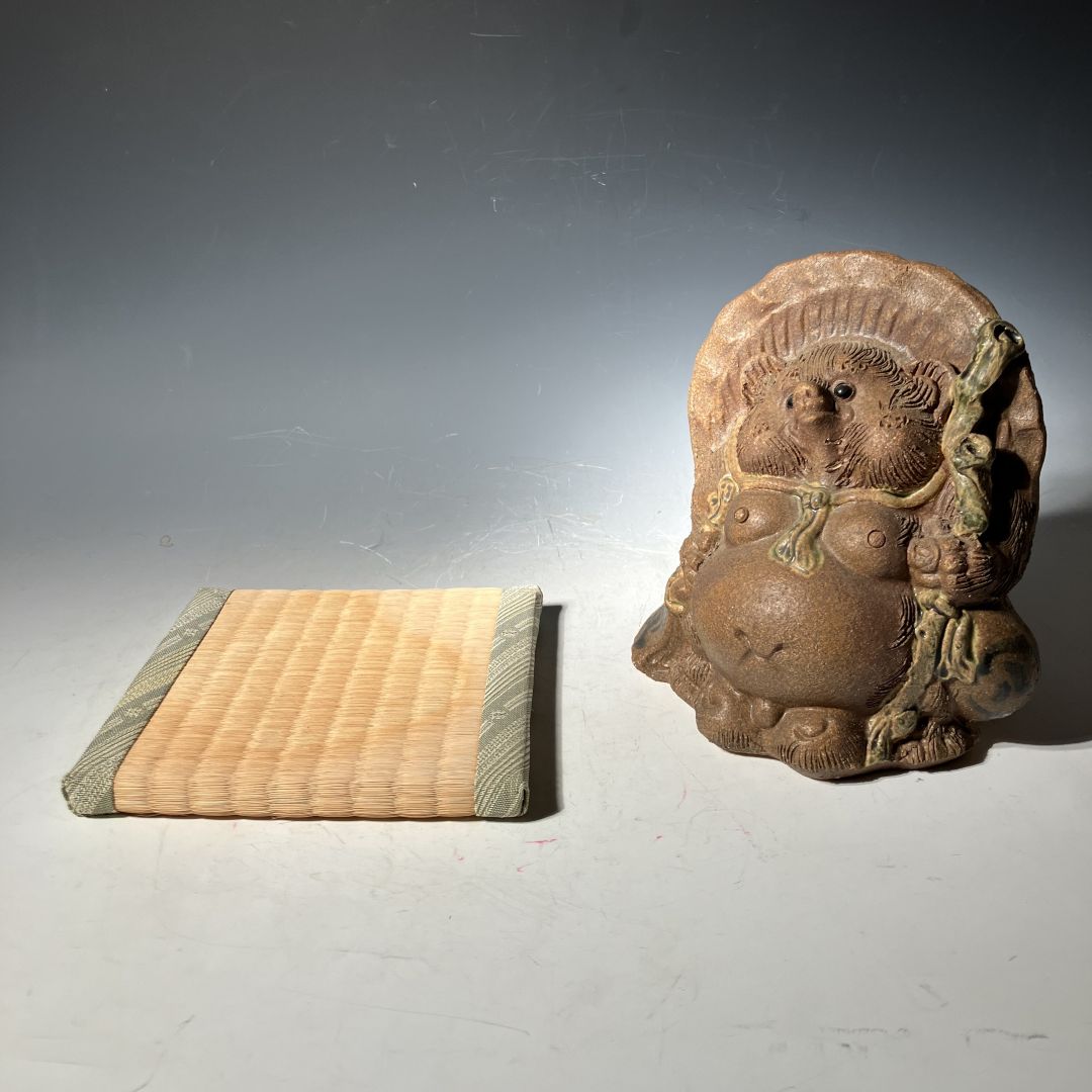 Ceramic sculpture of a bear with a woven mat on a gray background