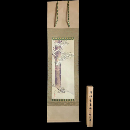 An East Asian hanging scroll depicts a plum tree in bloom with a decorative border, suspended by green cords, accompanied by a wooden box with East Asian script. The background is black.