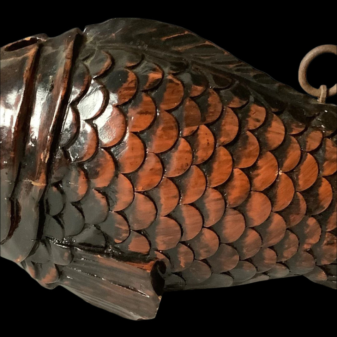 A close-up of the body of a wooden fish sculpture, showcasing its intricately carved and polished scales in a rich, dark brown hue with a lustrous sheen, accompanied by a metal ring for hanging, against a soft gray background.