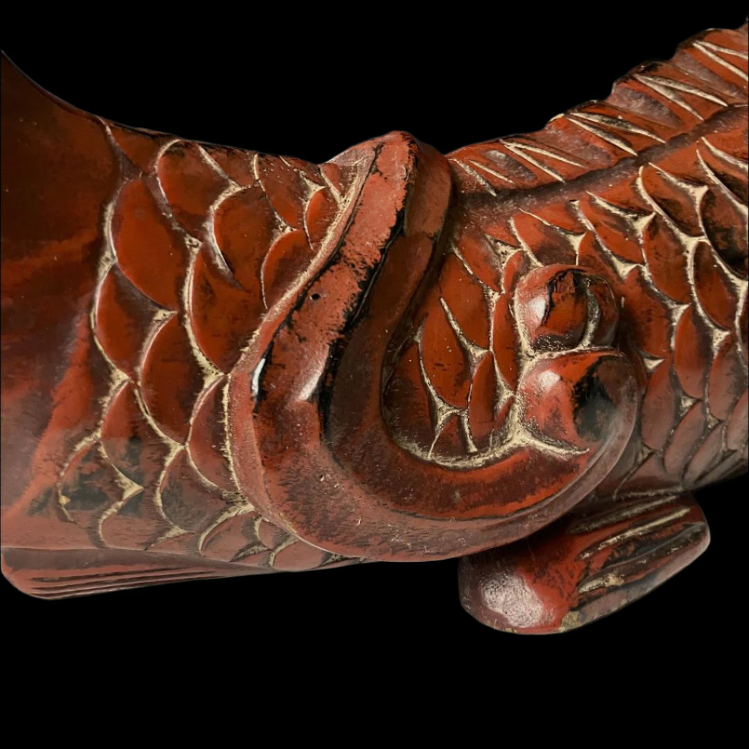 Close-up of the tail section of an antique wooden fish carving, highlighting the detailed scale pattern and the aged red-brown patina with black accents, along with the curved form and the weathered surface that adds to its antique character.