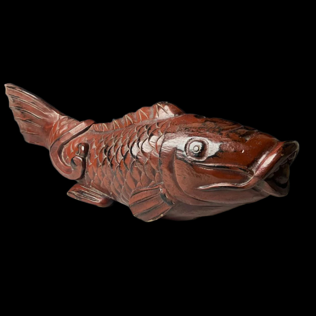 An antique Japanese kitchenware item, designed as a detailed wooden fish carving. The fish is predominantly brown with darker shading to accentuate its scales and features. The fish is positioned with the head and tail bent slightly upwards.