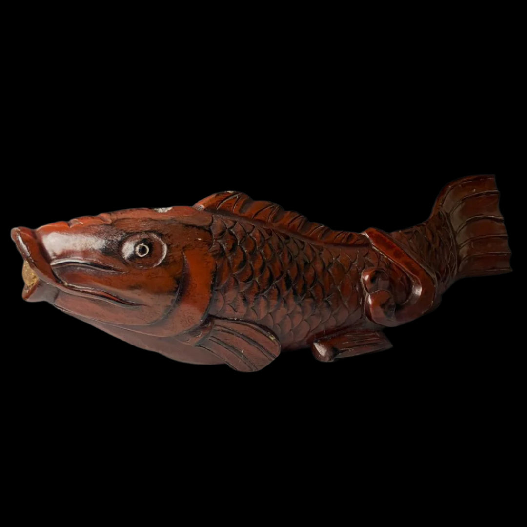 An antique Japanese kitchenware item, designed as a detailed wooden fish carving. The fish is predominantly brown with darker shading to accentuate its scales and features. The fish is positioned with the head and tail bent slightly upwards.