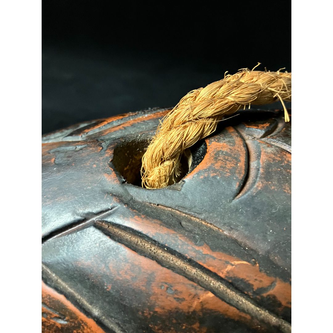 A thick rope is hanging from the head of a carved fish-shaped jizaikagi, a traditional Japanese fireplace crane used for suspending pots over an open fire. The fish head is intricately carved and serves as a decorative element. The rope is used to adjust the height of the pot over the fire.