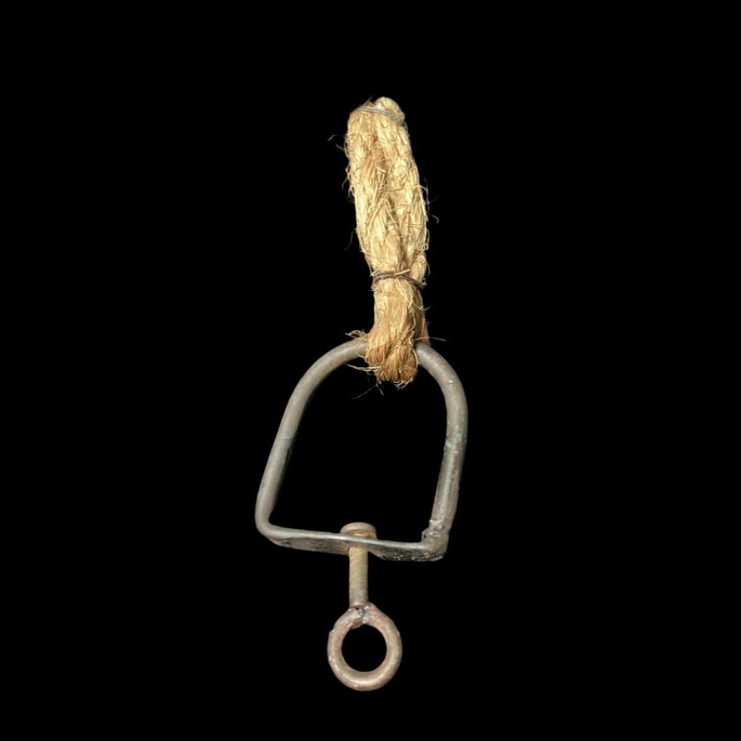 An iron device with a hook is attached to a thick rope, which is hanging from a jizaikagi. The jizaikagi is a traditional Japanese fireplace crane used to suspend pots over an open fire. The device and rope are used to adjust the height of the pot over the fire.