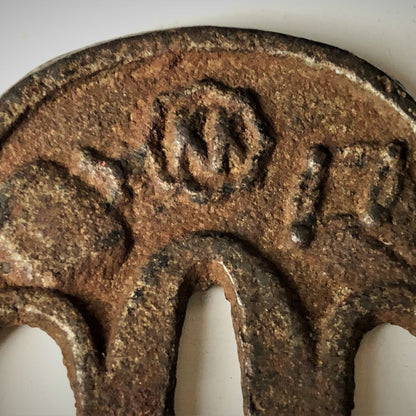 Close-up of a rusted metal object with engraved symbols on a white background