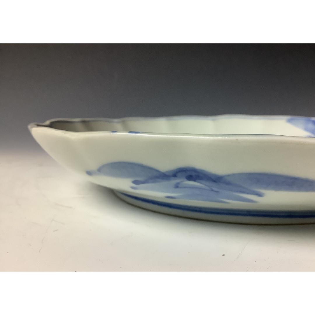 Side view of a scalloped-edge Japanese porcelain plate, with a glimpse of the painted blue landscape design on the interior against a neutral background.