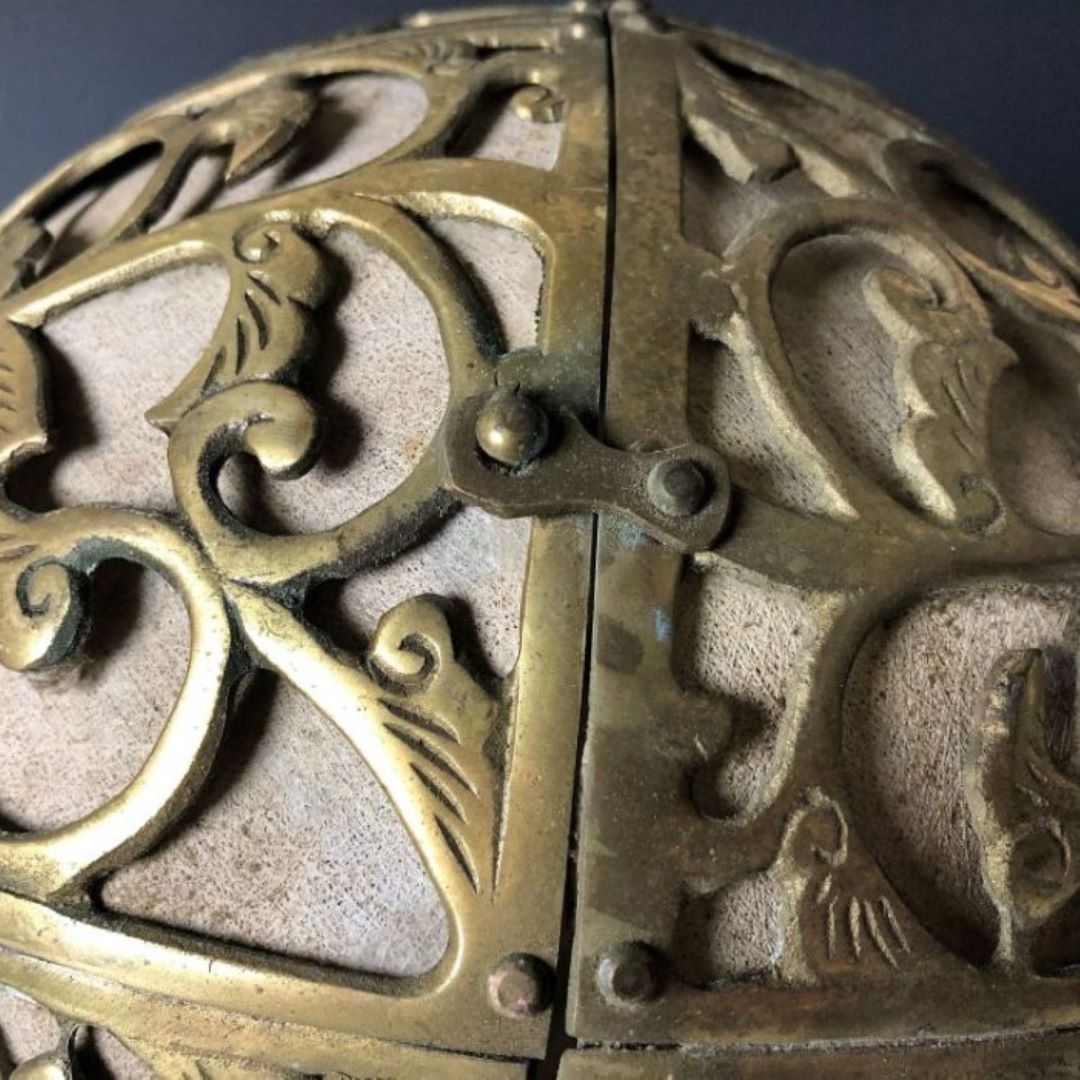 A close-up of the intricate pattern on a brass sphere with a focus on the ornamental filigree design, against a dark background.