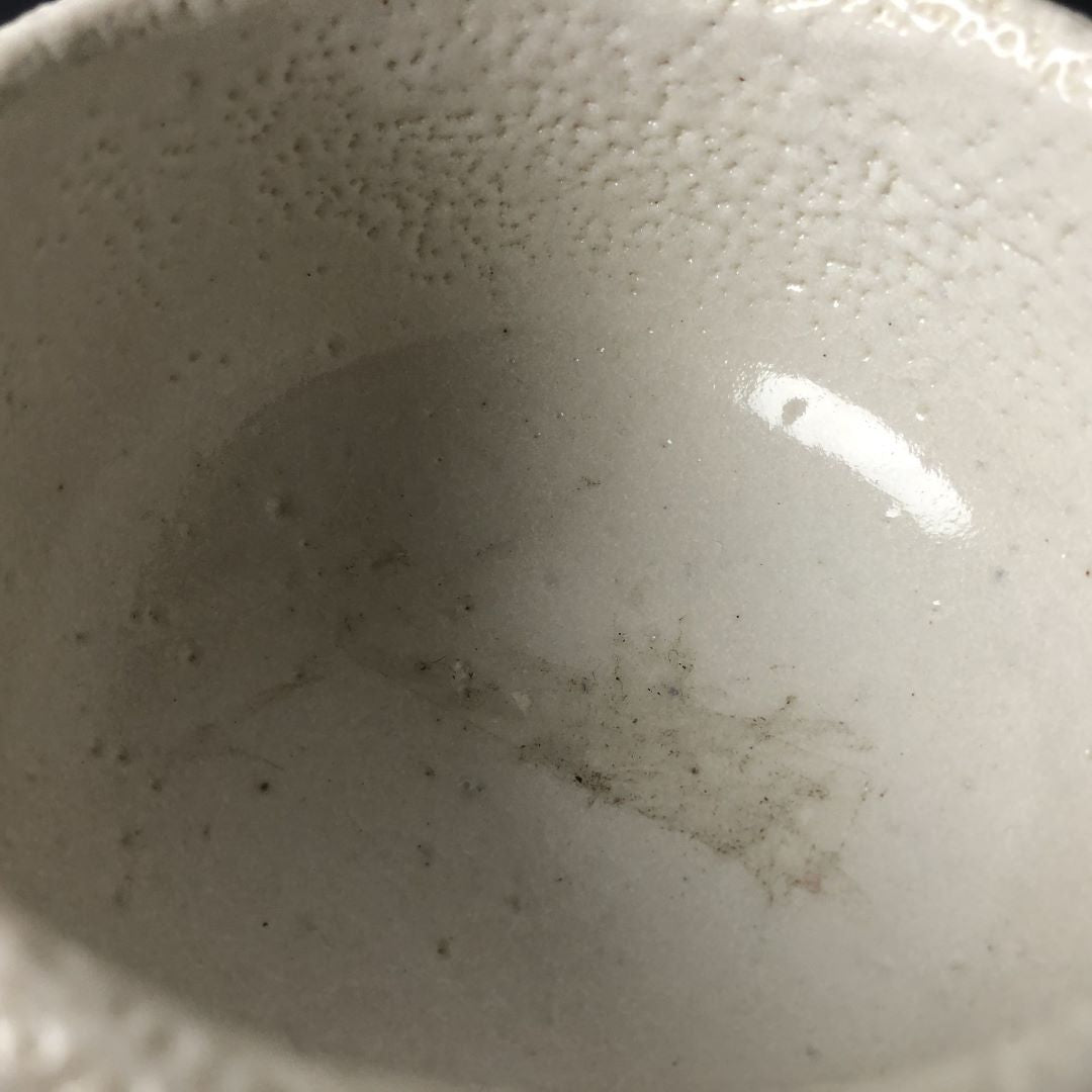 Close-up of the interior of a white Shino ware tea bowl showing its smooth glaze and subtle speckle texture, with natural variations and slight imperfections indicative of handcrafted pottery.