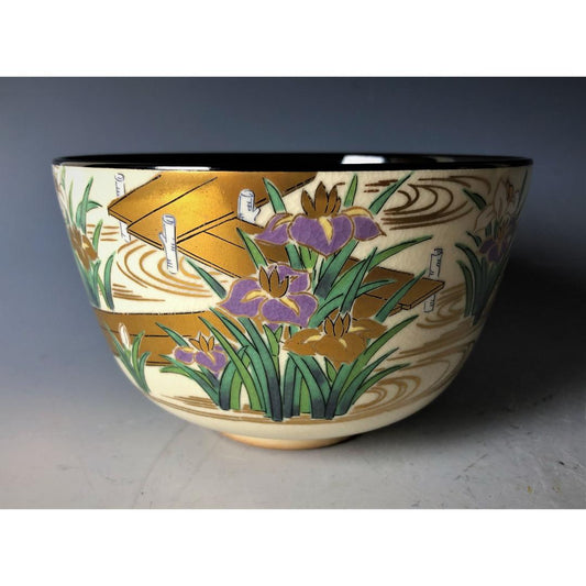 An ornate Kyo-yaki Japanese tea bowl, richly decorated with gold and purple iris patterns, showcasing the intricate craftsmanship against a soft grey backdrop.