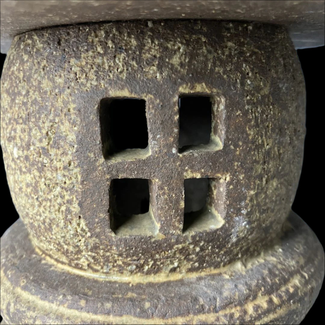 Close-up of the body of a vintage Japanese stone lantern, featuring square cut-out windows and a textured surface that highlights its traditional craftsmanship.