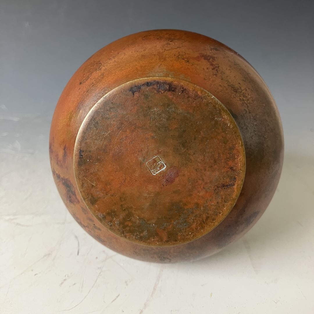 Bottom view of a copper vase showing the patina and maker's mark on its base.