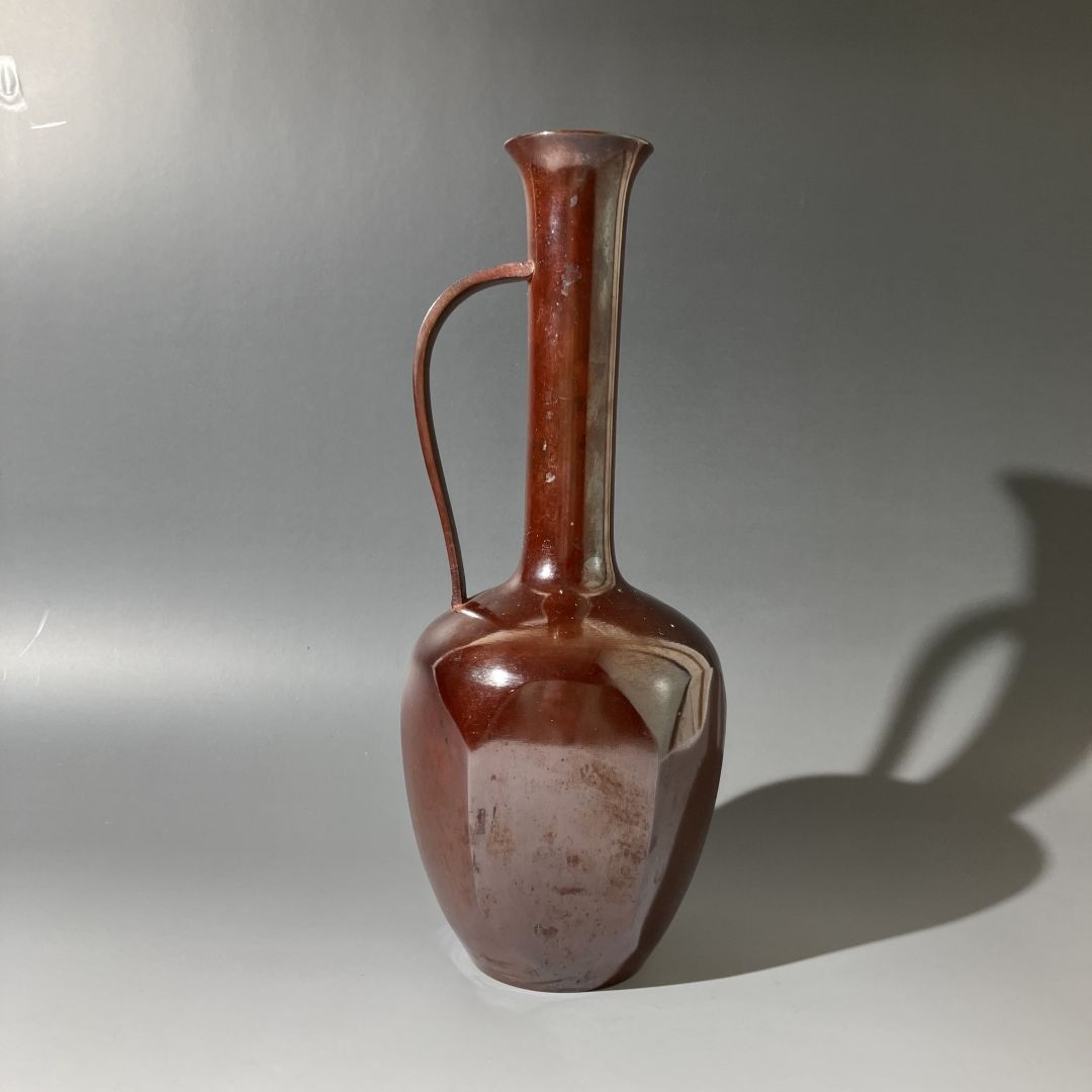Brown ceramic vase with a handle on a gray background