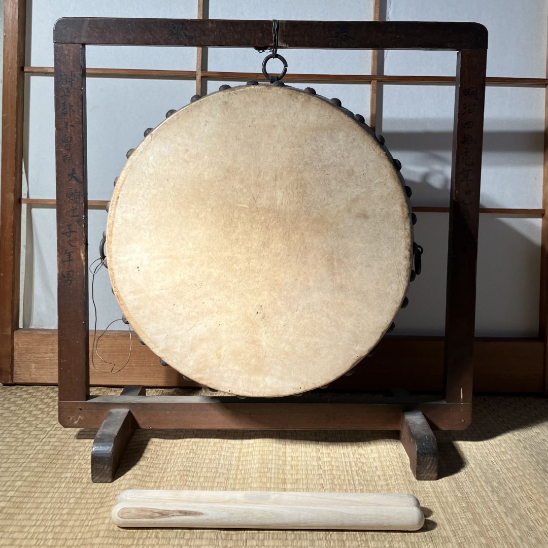 Traditional Japanese gong on a stand with a wooden handle on a tatami mat.