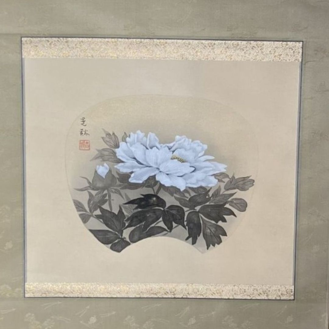 Framed artwork of a white flower with black leaves on a beige background