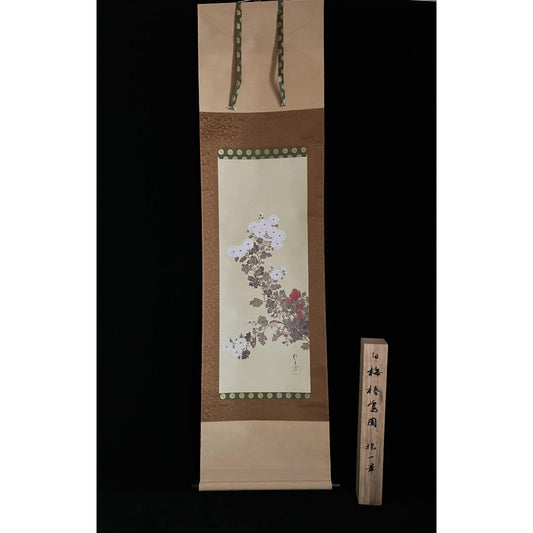  A hanging scroll with a floral painting, bordered by patterned fabric, displayed next to a wooden plank with Japanese characters, all against a black background.