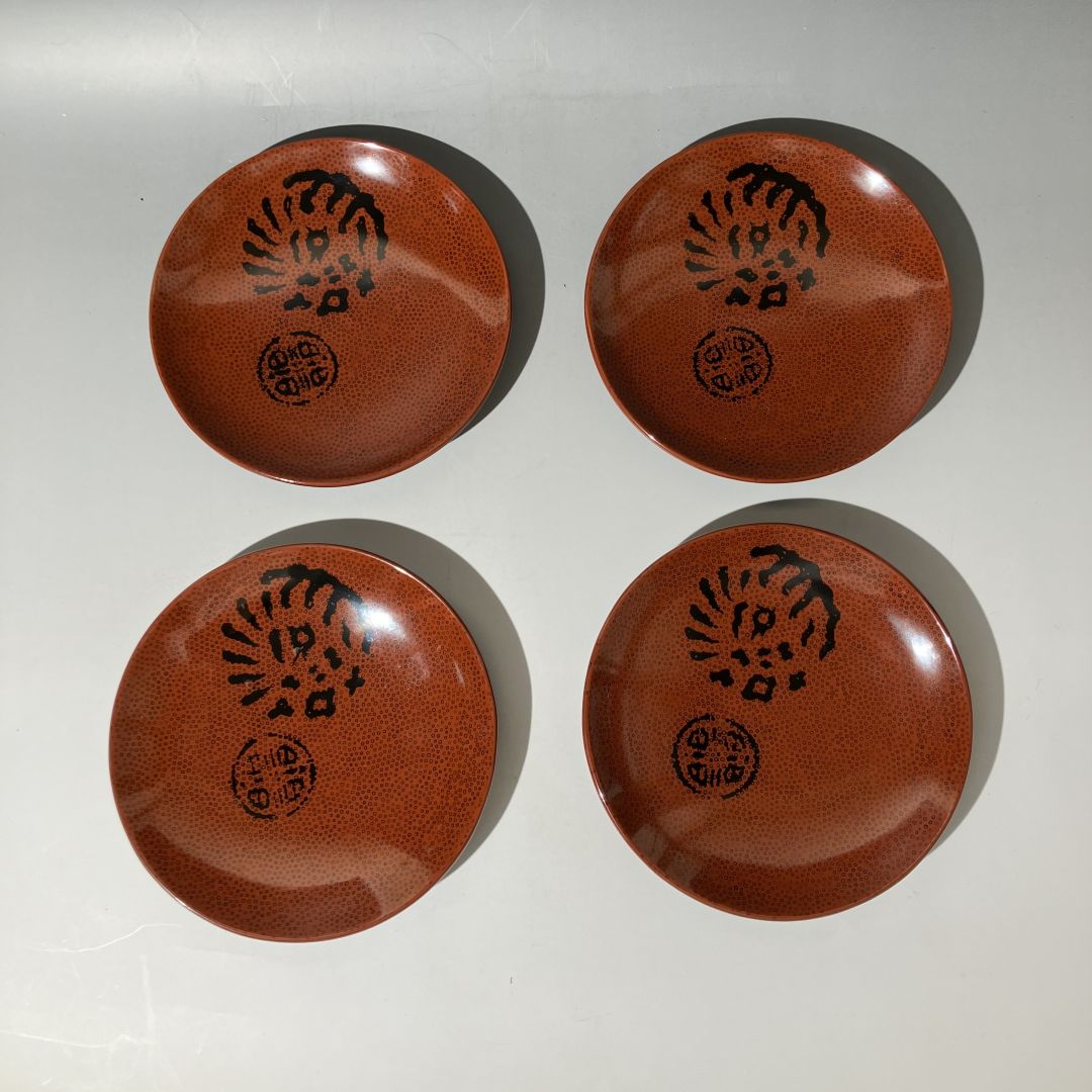 Four brown ceramic plates with black patterns on a white background