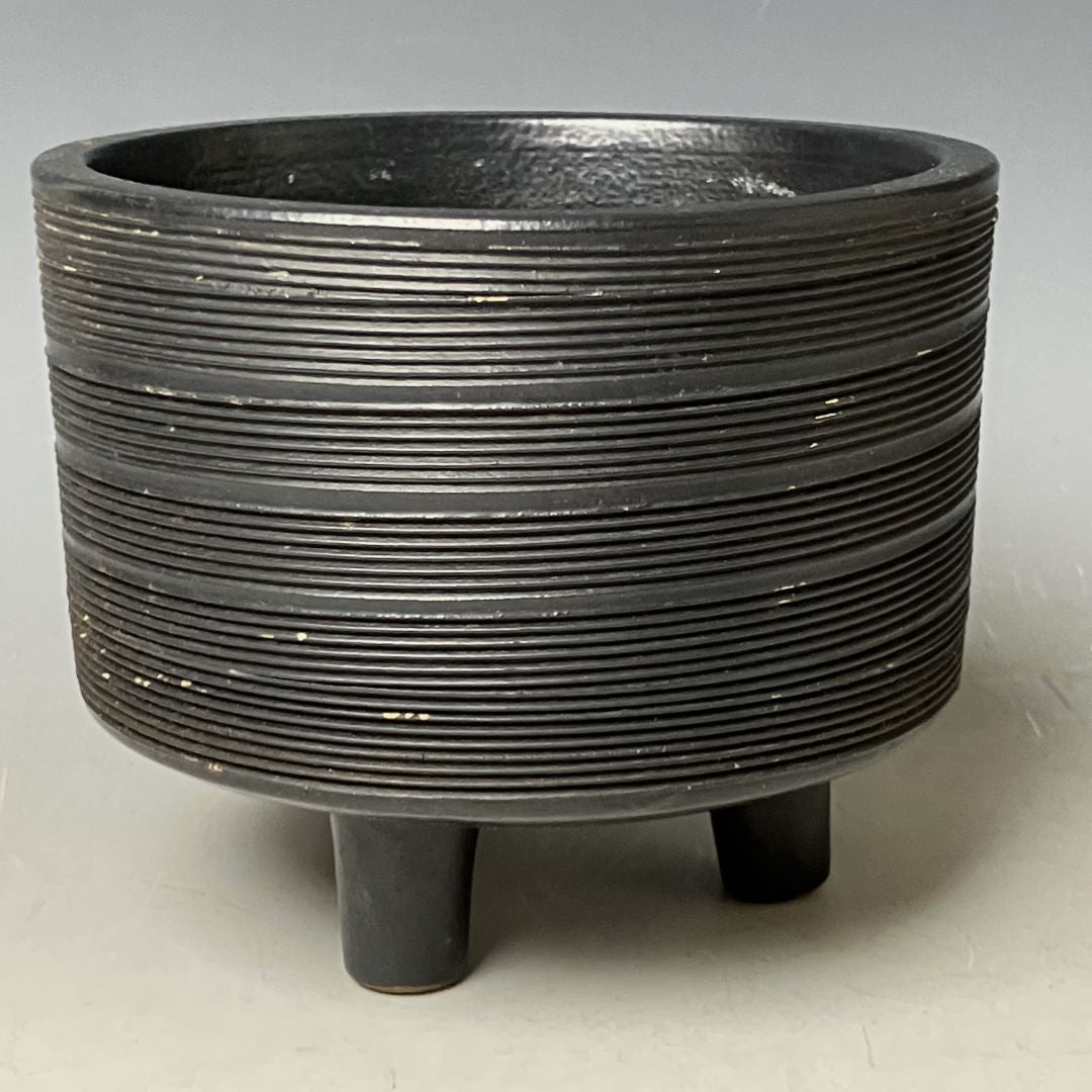 Black ribbed planter with three legs on a light gray background