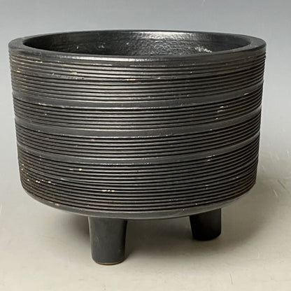 Black ribbed planter with three legs on a light gray background