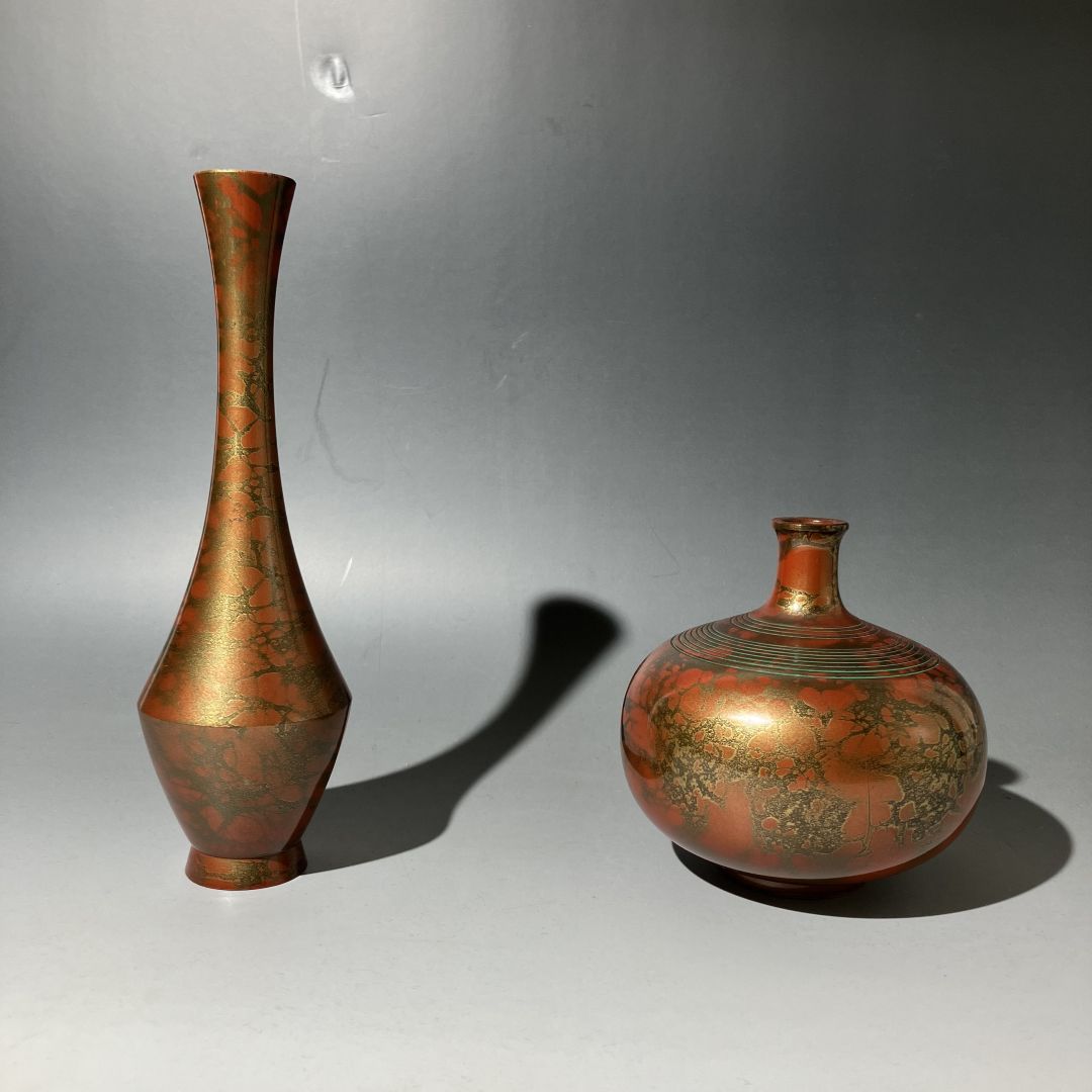 Two bronze vases with intricate designs on a gray background