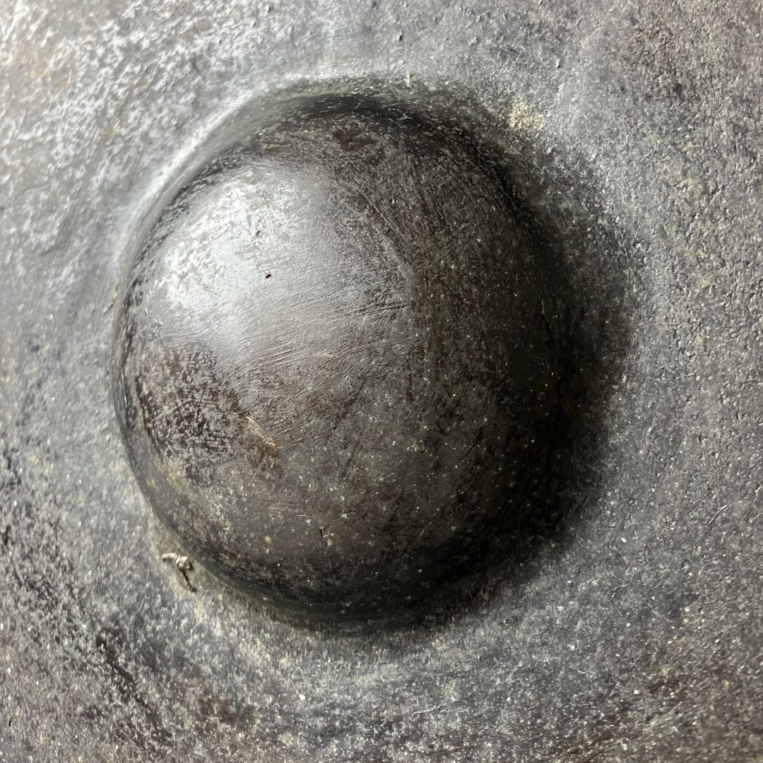 Macro view of the edge of a metallic iron gong showing its thick, curved profile with a textured, scratched surface, indicative of age and use.