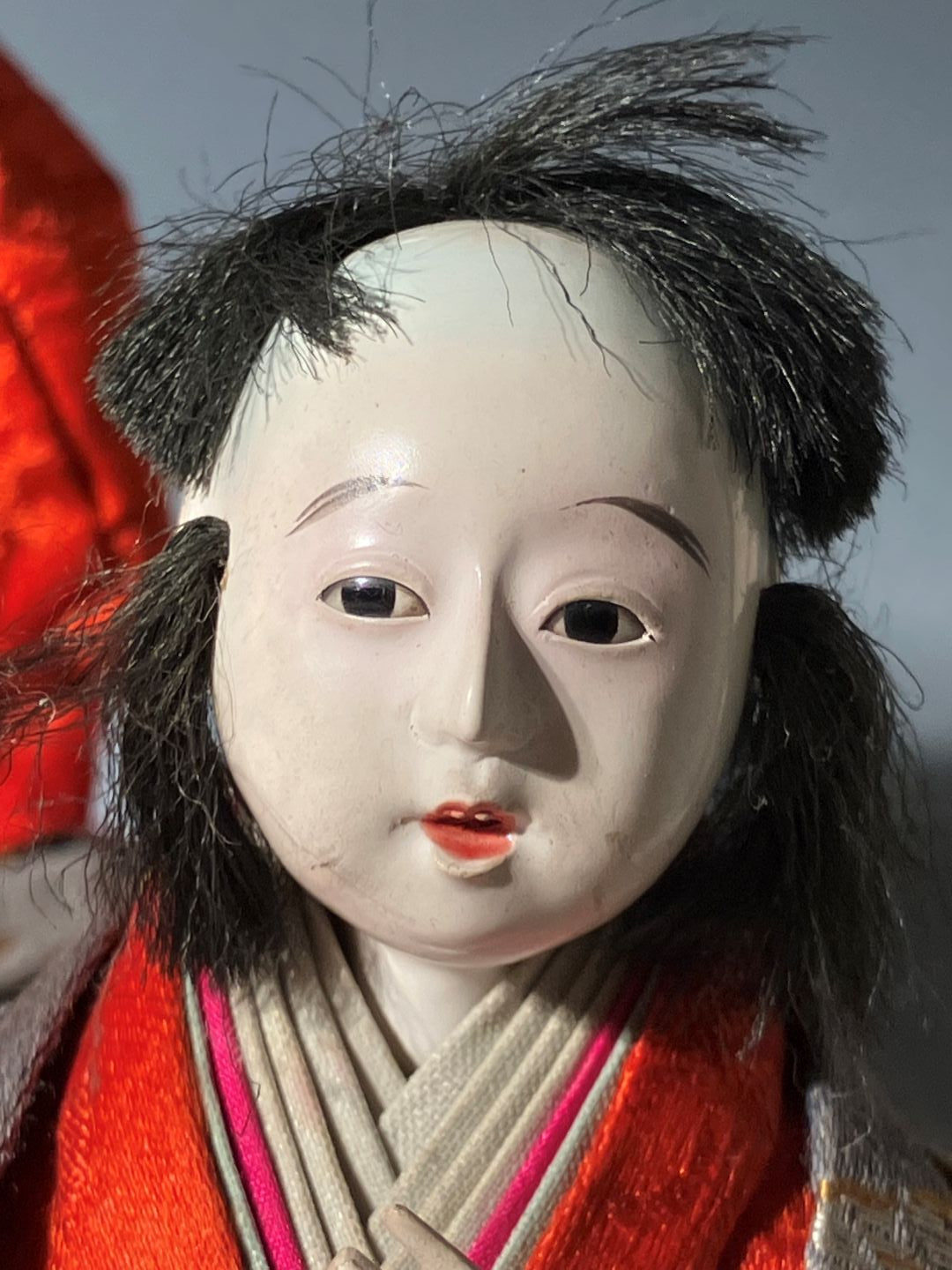 Close-up of a traditional doll with black hair and red clothing against a gray background