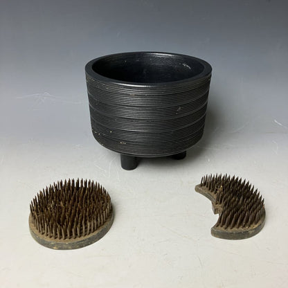 Black ribbed pot with two wooden bristle brushes on a gray background