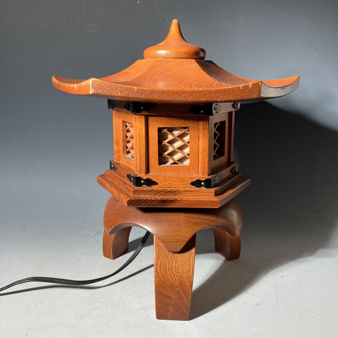 Vintage Japanese wooden pagoda-style lantern lamp handcrafted with lattice windows and curved roof, featuring black metal details and an electric cord, displayed against a neutral background.