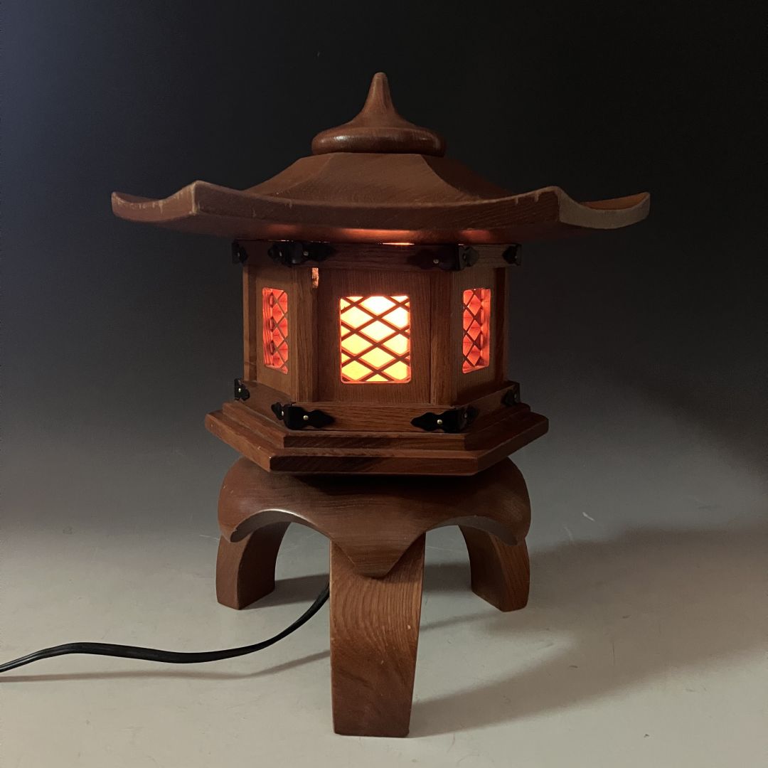 Vintage Japanese wooden pagoda lantern lamp illuminated with a warm amber light, showcasing lattice windows, curved roof, and elegant black metal accents, creating a serene and traditional atmosphere.