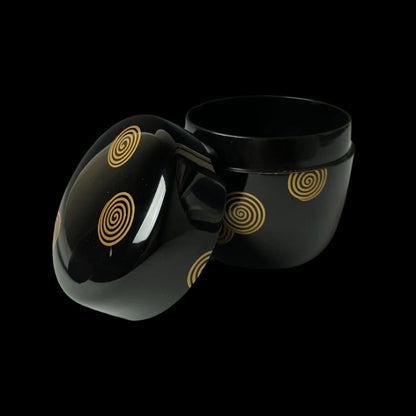 An open 19th-century Japanese lacquered makie natsume tea caddy, displaying its black finish adorned with gold spiral designs, highlighting the intricate craftsmanship and elegance of traditional Japanese tea ware.
