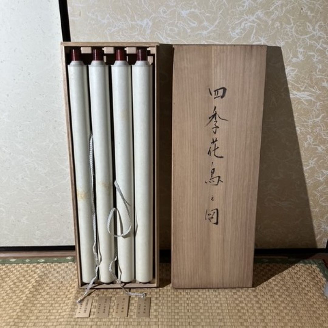 Wooden box with three cylindrical items inside, set against a textured wall.