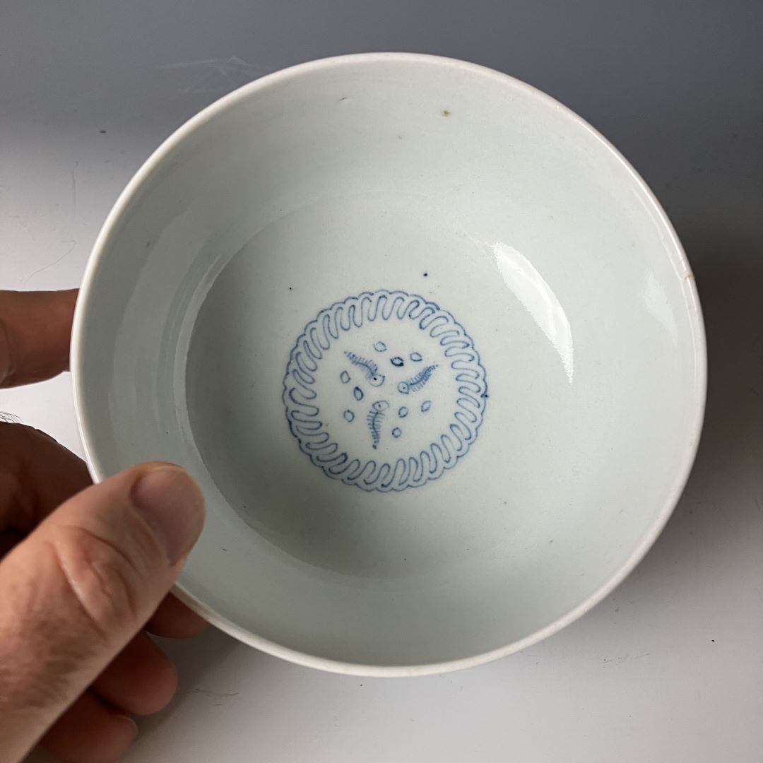 A person holding a 19th-century Japanese Ko-Imari porcelain bowl, showcasing the interior design featuring a delicate blue circular pattern with floral elements at the center on a glossy white background.