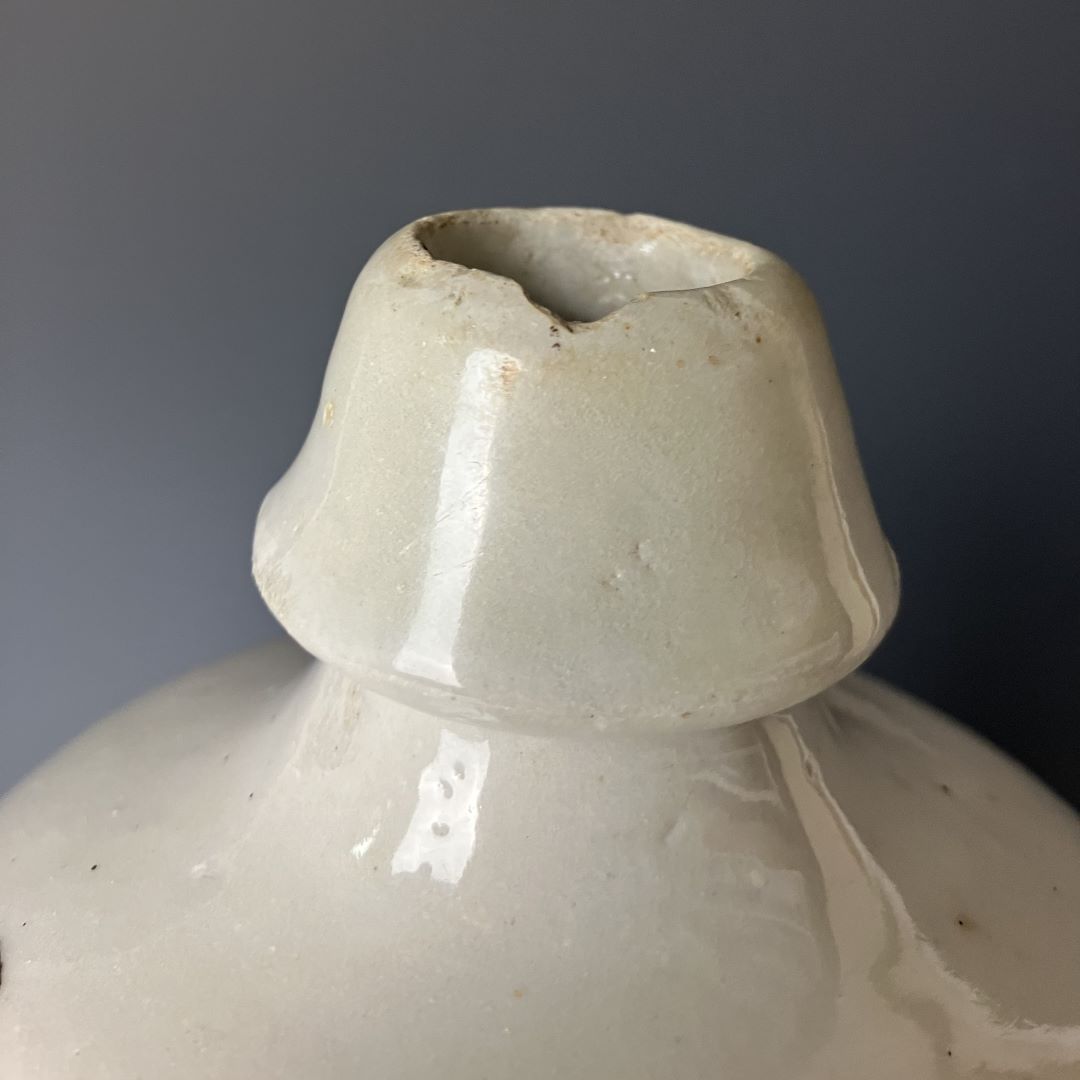 The image shows a close-up of the top of an antique Japanese ceramic sake bottle (Tokkuri), focusing on the spout. The spout appears chipped, highlighting the bottle's vintage character against a muted background.