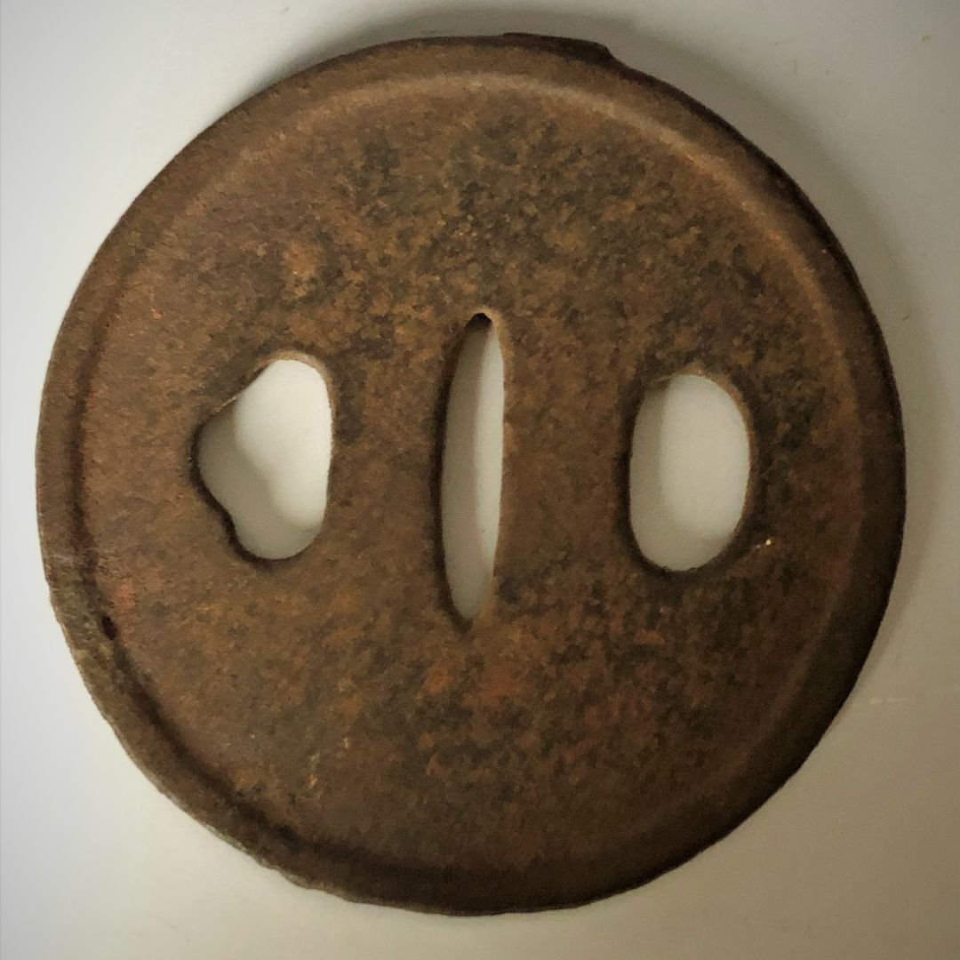 Rust-colored metal tsuba with three white stones on a white background