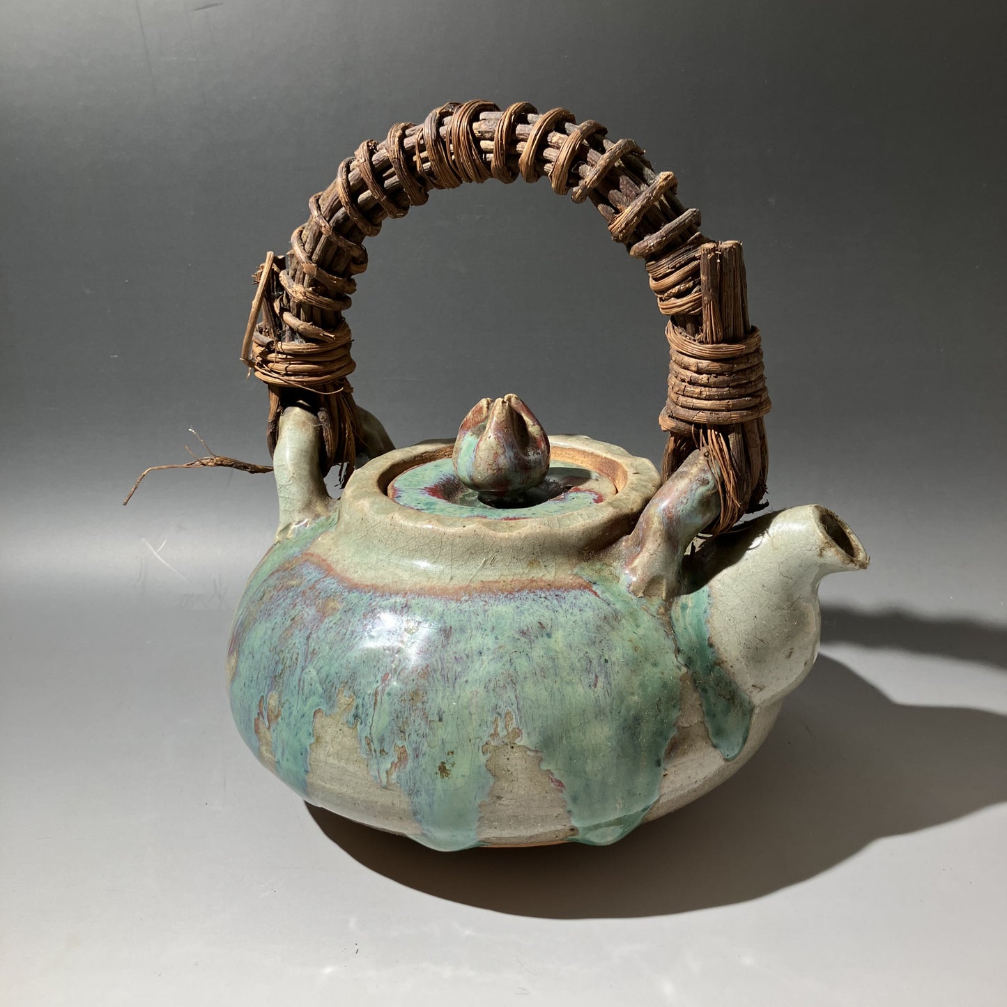 Ceramic teapot with wicker handle on a gray background