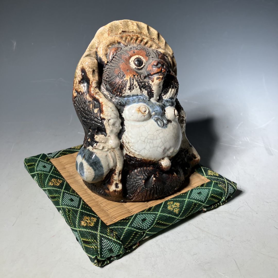 Ceramic owl figurine on a green patterned cushion with a gray background