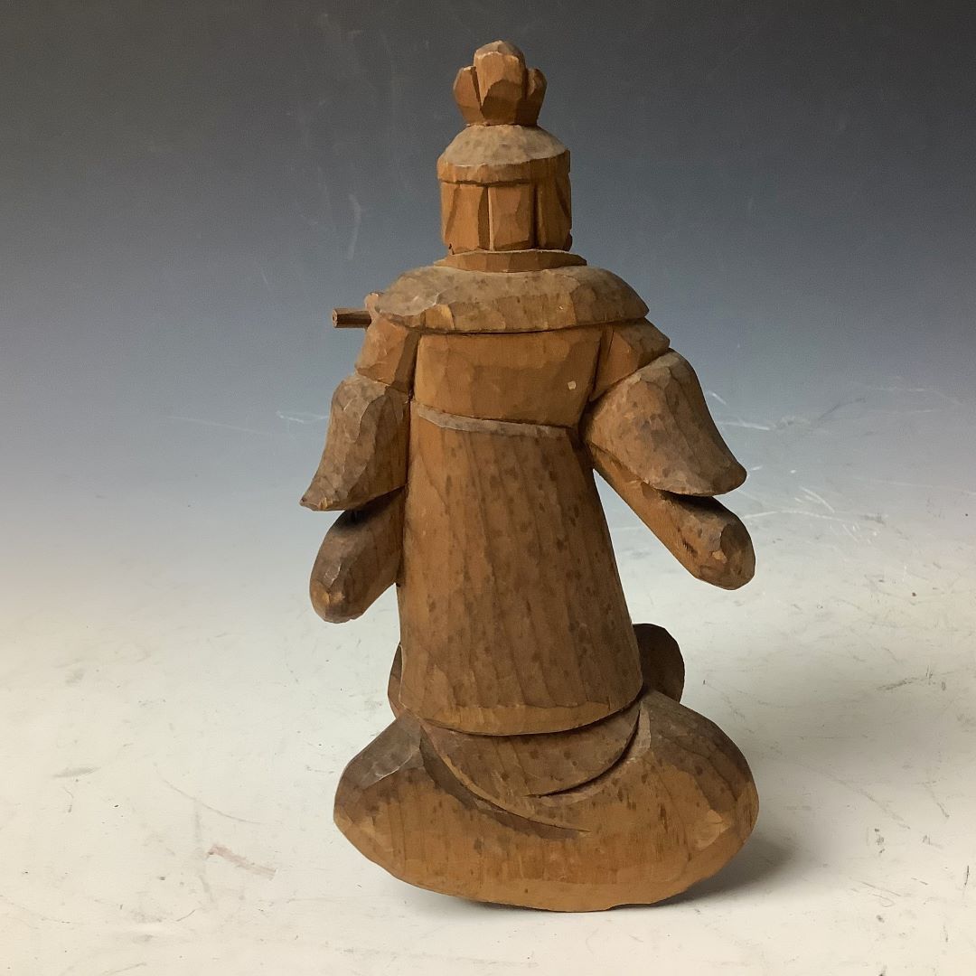 A rear view of a wooden sculpture of Komokuten, a Japanese Buddhist guardian deity, standing 14 cm tall, carved with a flowing robe and a traditional headdress, exhibiting detailed textures and natural wood grain.