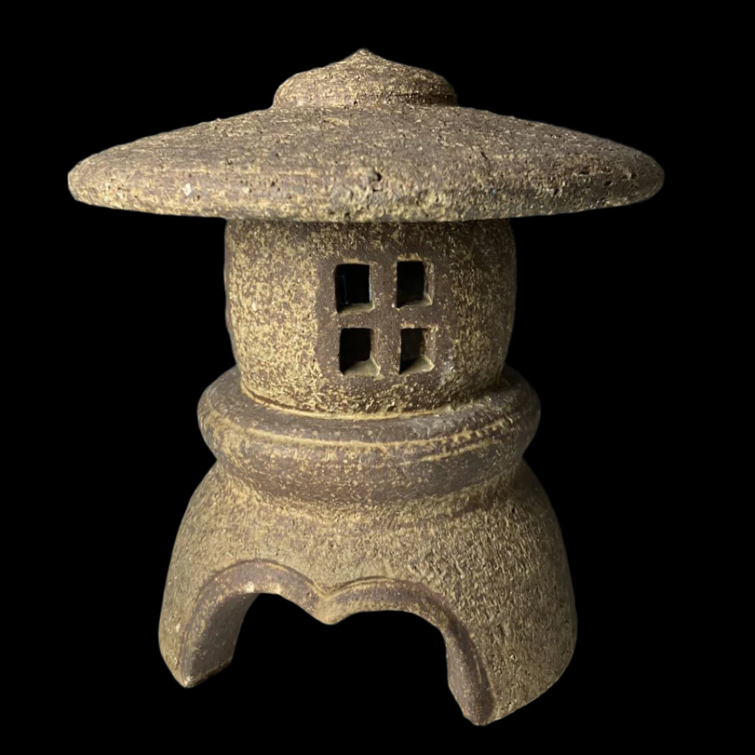 Close-up of a vintage Japanese stone lantern with a domed roof, square cut-out windows, and a textured surface, showcasing traditional craftsmanship and rustic charm.