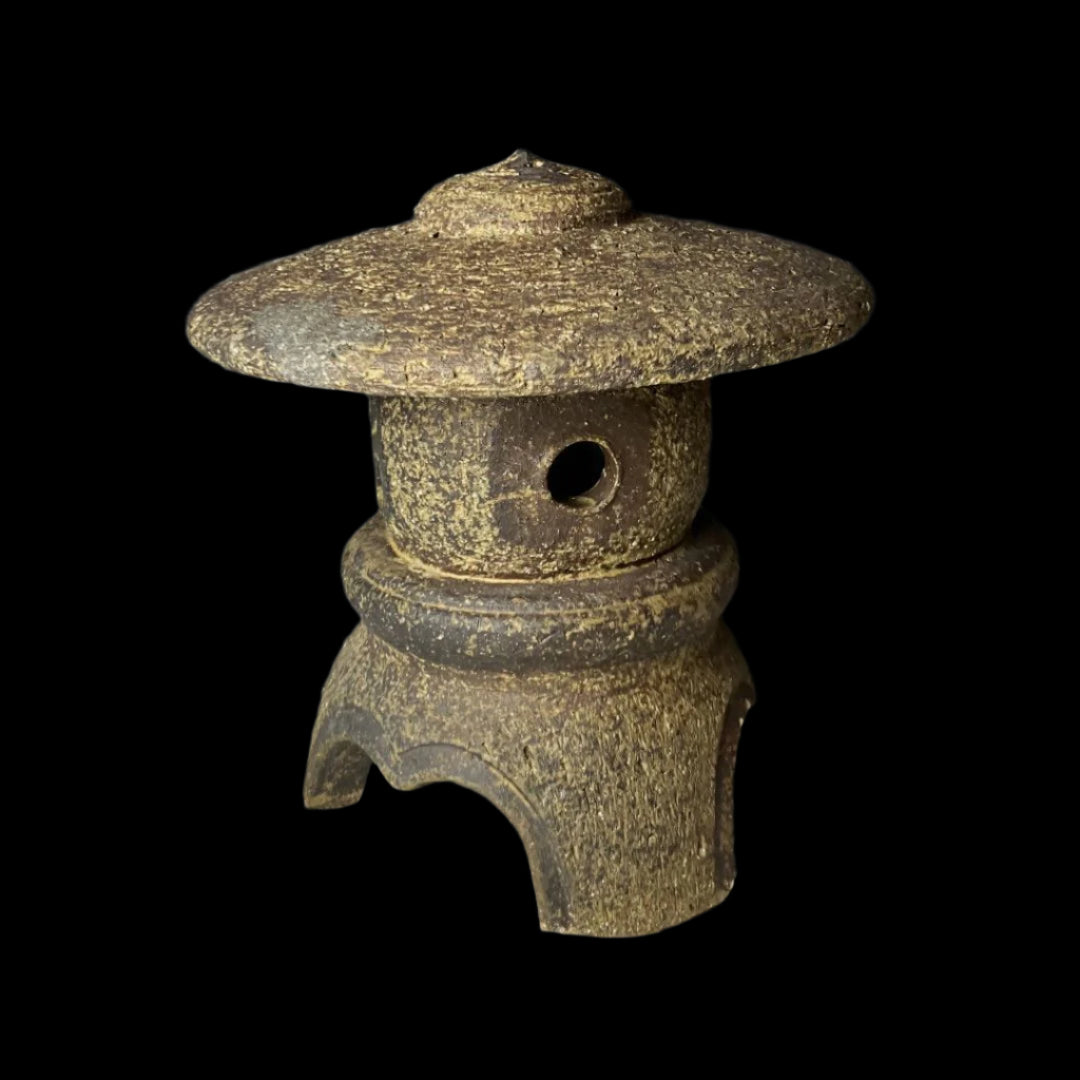 Close-up of a vintage Japanese stone lantern with a domed roof, square cut-out windows, and a textured surface, showcasing traditional craftsmanship and rustic charm.