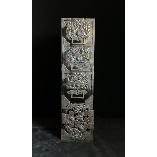 A Japanese tansu cabinet with silver mythical elements reliefs on its drawers, set against a black background.