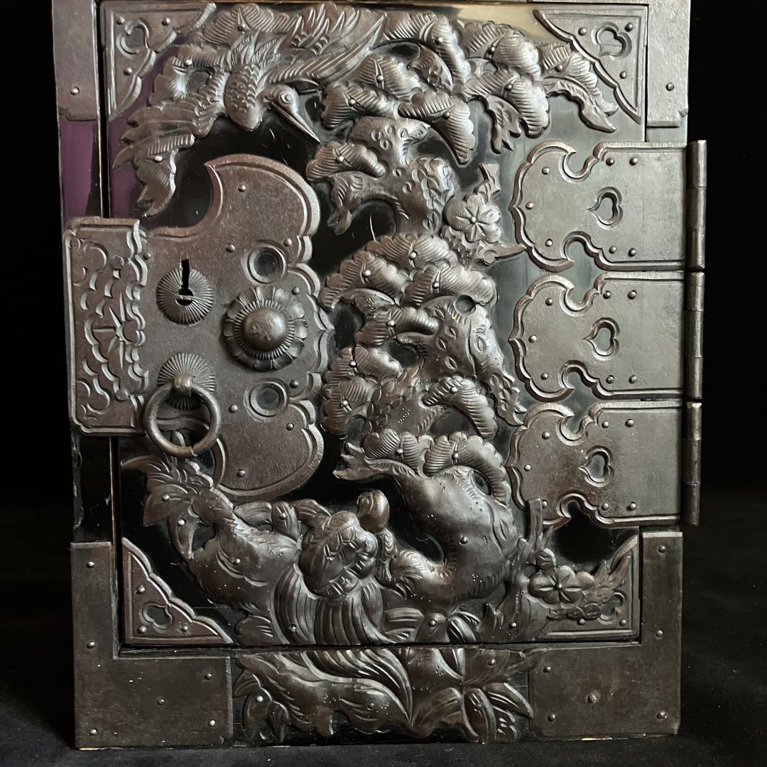 Close-up of a Japanese tansu cabinet drawer with intricate silver-tone metalwork depicting a three-dimensional dragon surrounded by clouds, with traditional metal hardware and hinges visible.